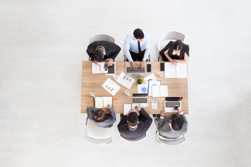 Aerial view of professionals working at a conference table covered in laptops, notebooks, and documents, representing the Toronto business litigation lawyers at Milosevic & Associates and their advice in shareholder disputes.