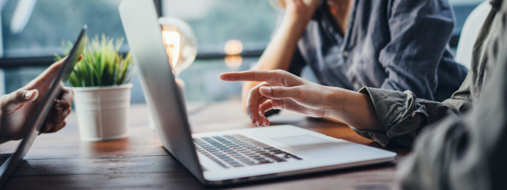 Close-up of a group of professionals working at a table together and pointing at a laptop screen, representing the Toronto business litigation lawyers at Milosevic & Associates and their representation in defamation, libel, and slander claims.