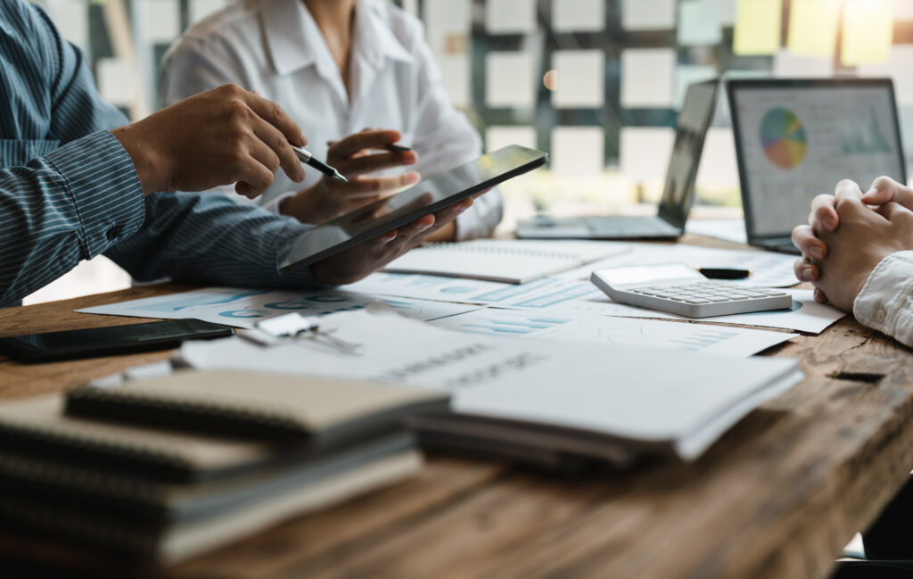 Three business people sitting at a desk and working on financial projections with a tablet, laptop, and calculator, representing the investment loss and investment fraud litigation services provided by Milosevic & Associates in Toronto.