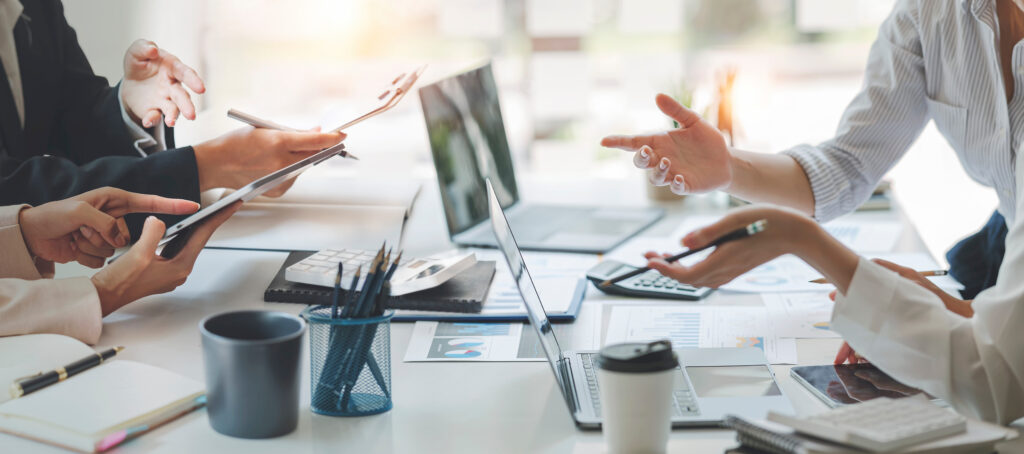 A group of professionals talking over a table full of laptops, tablets and documents, representing claims arising from investment loss and investment fraud, provided by the Toronto litigation lawyers at Milosevic & Associates.