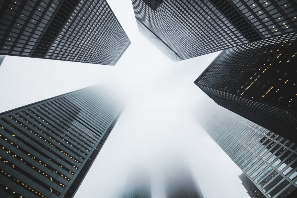 black and white image from below looking up at imposing office towers partially obscured by fog near the top