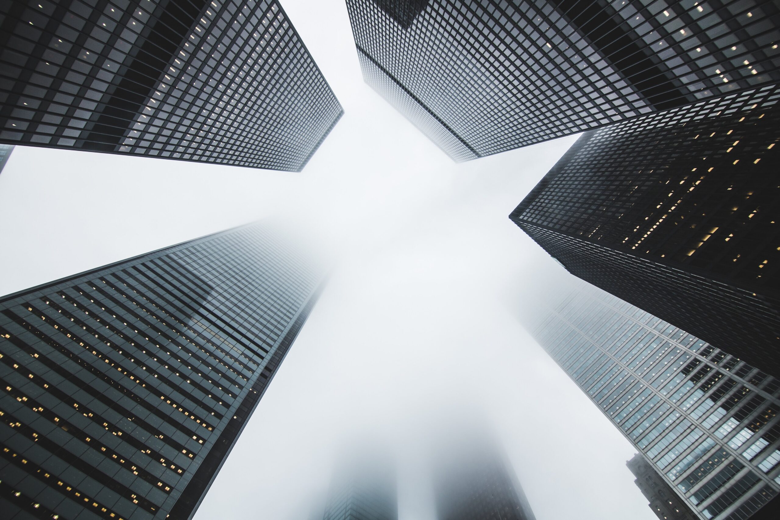 black and white image from below looking up at imposing office towers partially obscured by fog near the top