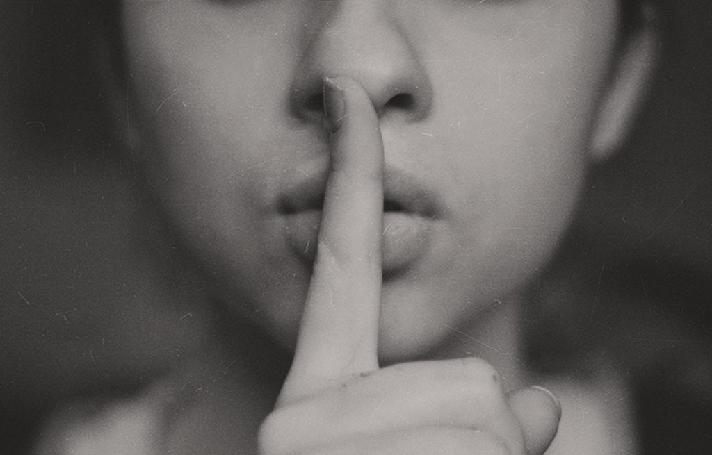 a woman holding her finger to her lips as if to represent staying silent