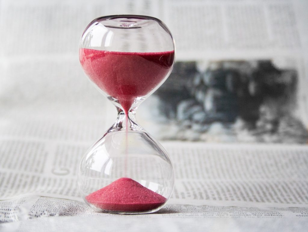 A clear hourglass with red sand falling through, representing the period of reasonable discoverability in a civil action.