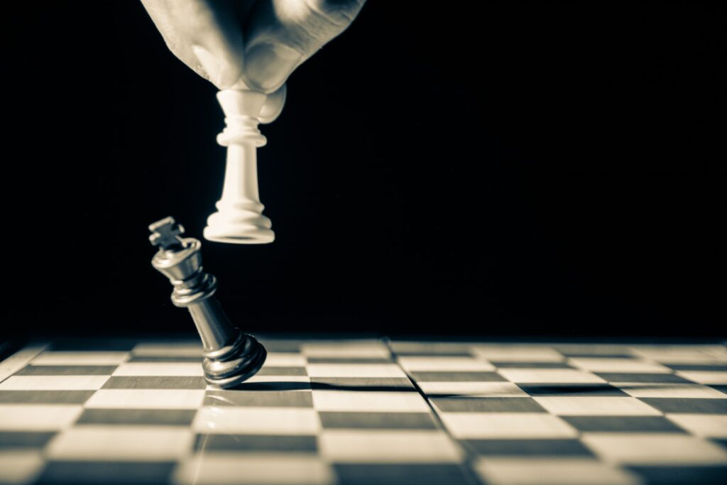 A white pawn knocking over a black King on a chessboard, representing partisanship in politics