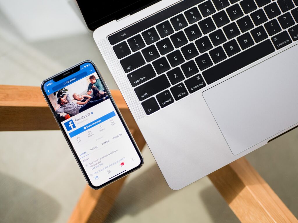 iPhone x beside mac book with facebook on iPhone screen