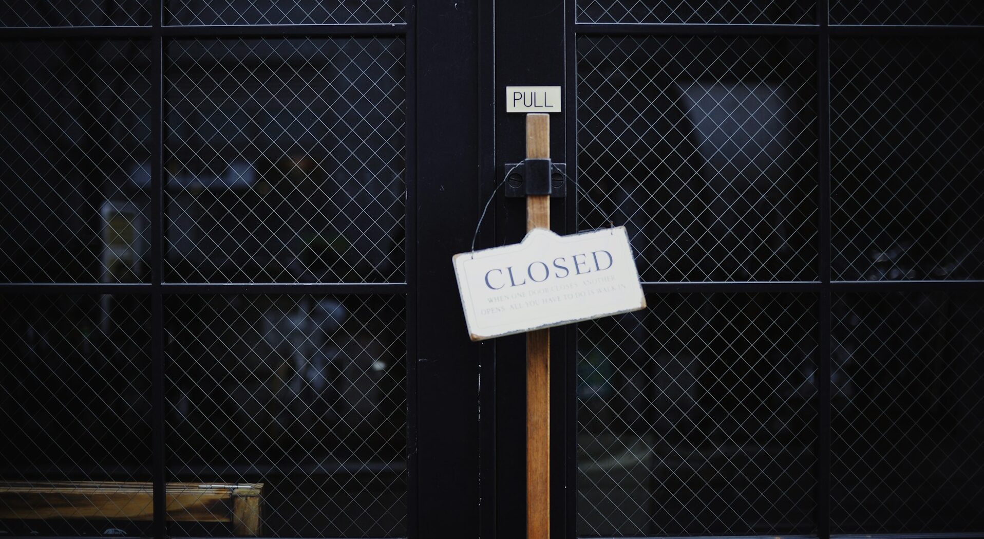 A black industrial mesh gate that is locked with a white "Closed" sign, representing a business shut-down or winding up a corporation