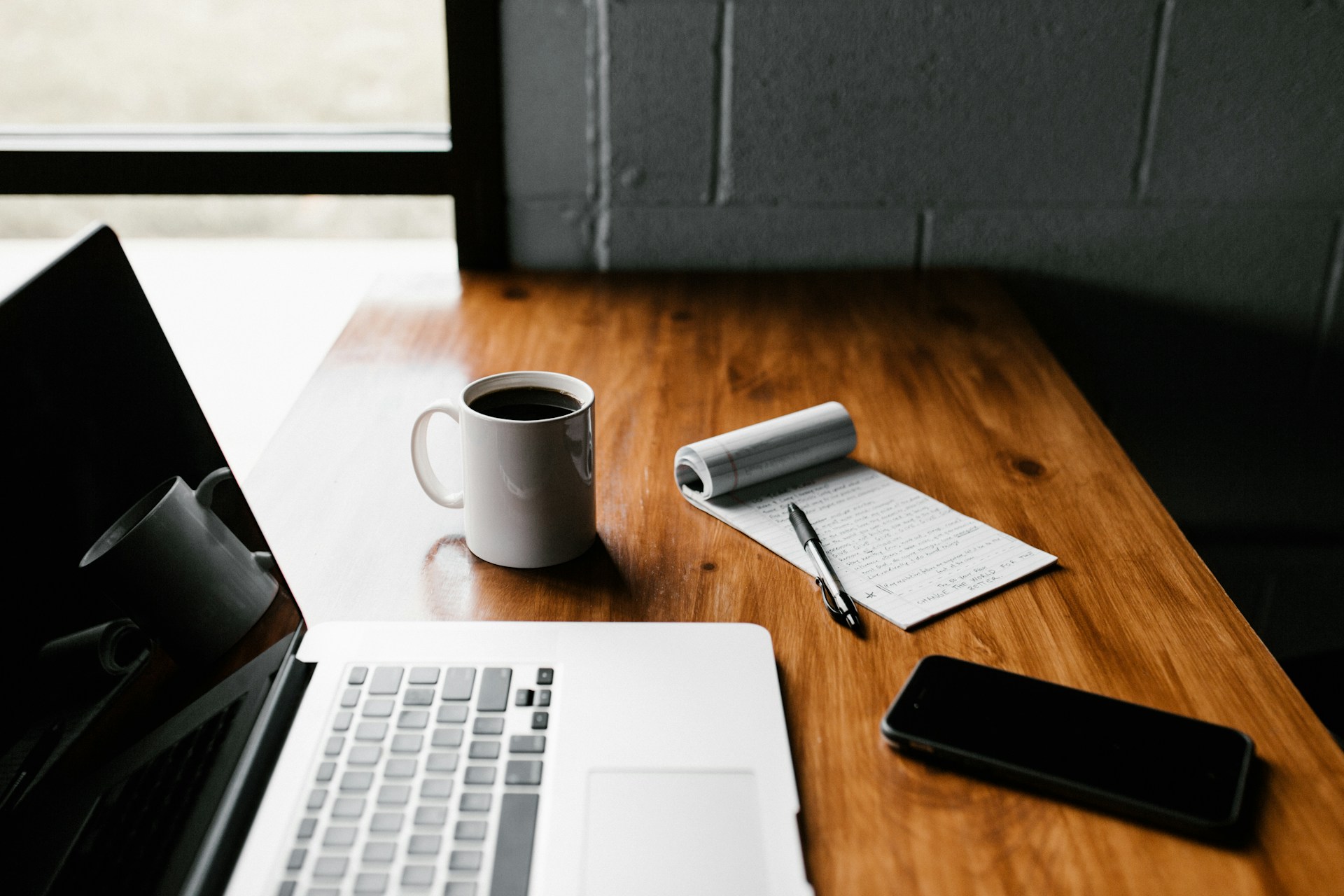 A macbook, notebook and coffee mug on a desk, representing absolute privilege and defamation claims