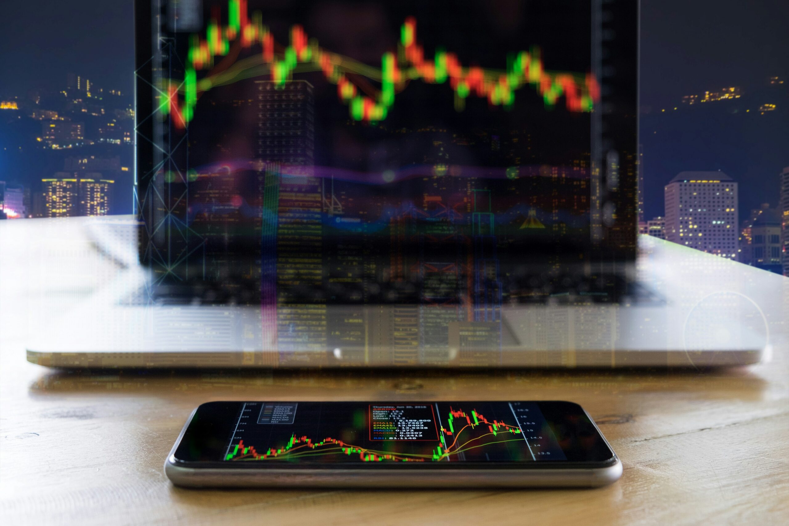 Close up of a laptop and cell phone displaying share prices with a window overlooking a city in the background, representing shareholder disputes and the oppression remedy in Ontario