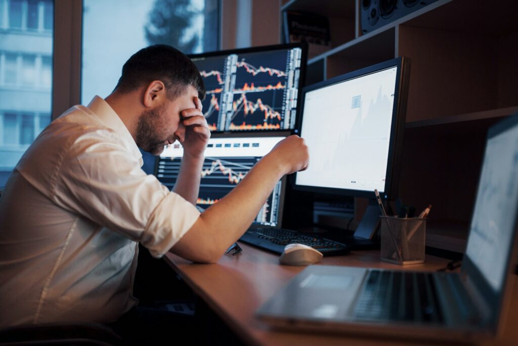 A dejected man sitting at a computer with his head in his hand, representing Ponzi schemes.