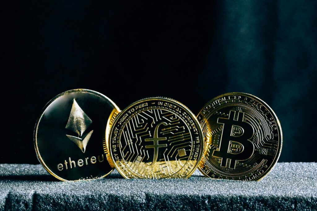 Three gold crypto coins are balanced on edge and overlapping each other on a gray textured surface and against a black background, representing the company responding to the Ontario Securities Commission summons.