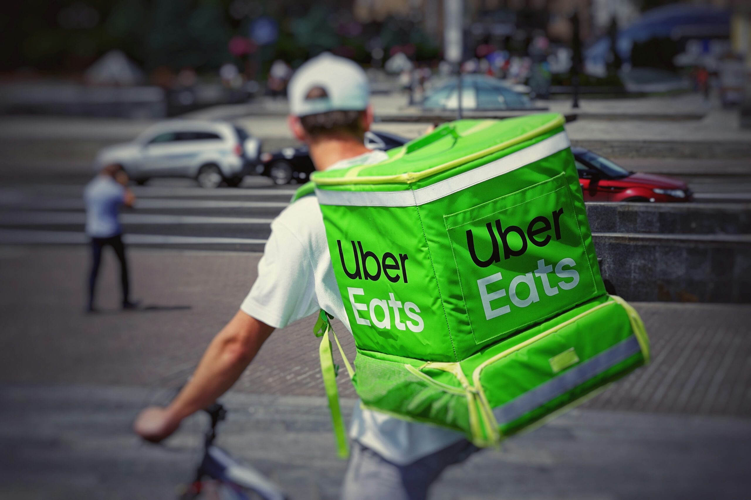 A man with a green Uber Eats bag strapped to his back looks out over a busy city roadway, representing Uber Canada arbitration clause.