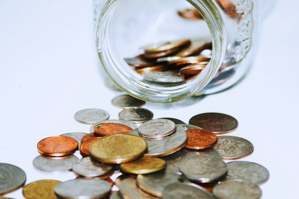 A glass jar filled with coins on its side, with coins spilled out beside it, representing Guarantees.