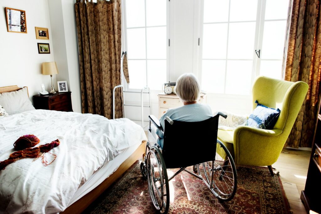 An elderly woman in a wheelchair, looking out of the window of a long-term care facility, representing defamation and anti-SLAPP claims and the allegations in the Universalcare Canada v. Gusciglio case