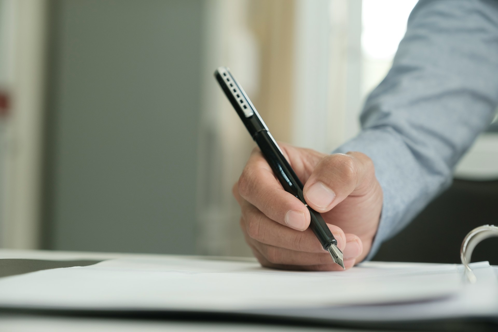 A man's hand signs a contract with a black fountain pen, representing anticipatory breach and contract repudiation.